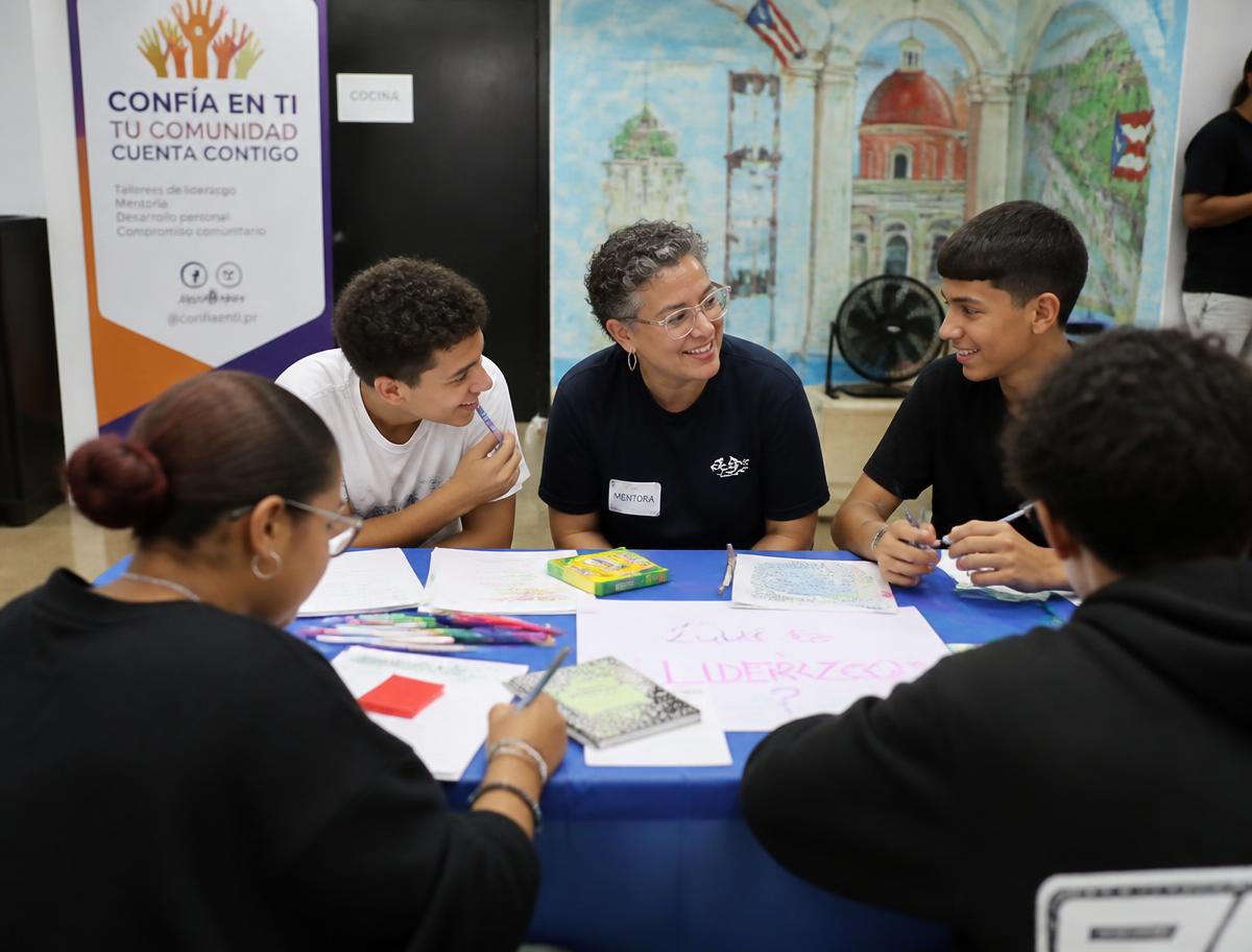 A mentor working with teenagers around a table during a leadership workshop